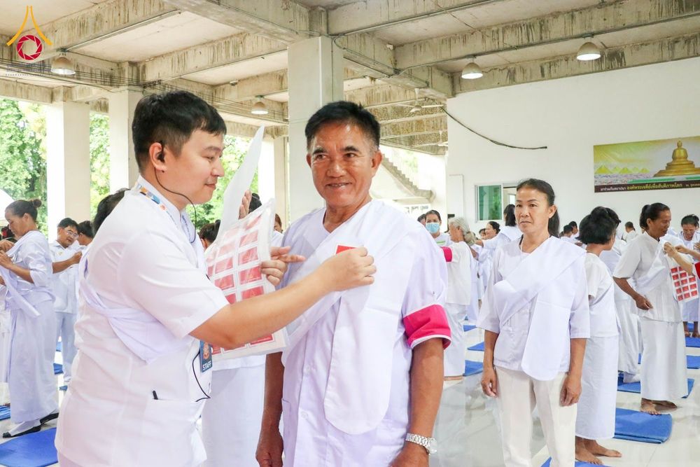 เจ้าหน้าที่กำลังติดป้ายสัญลักษณ์บนเสื้อให้ผู้ชายวัยกลางคนในชุดสีขาวภายในโครงการอบรม