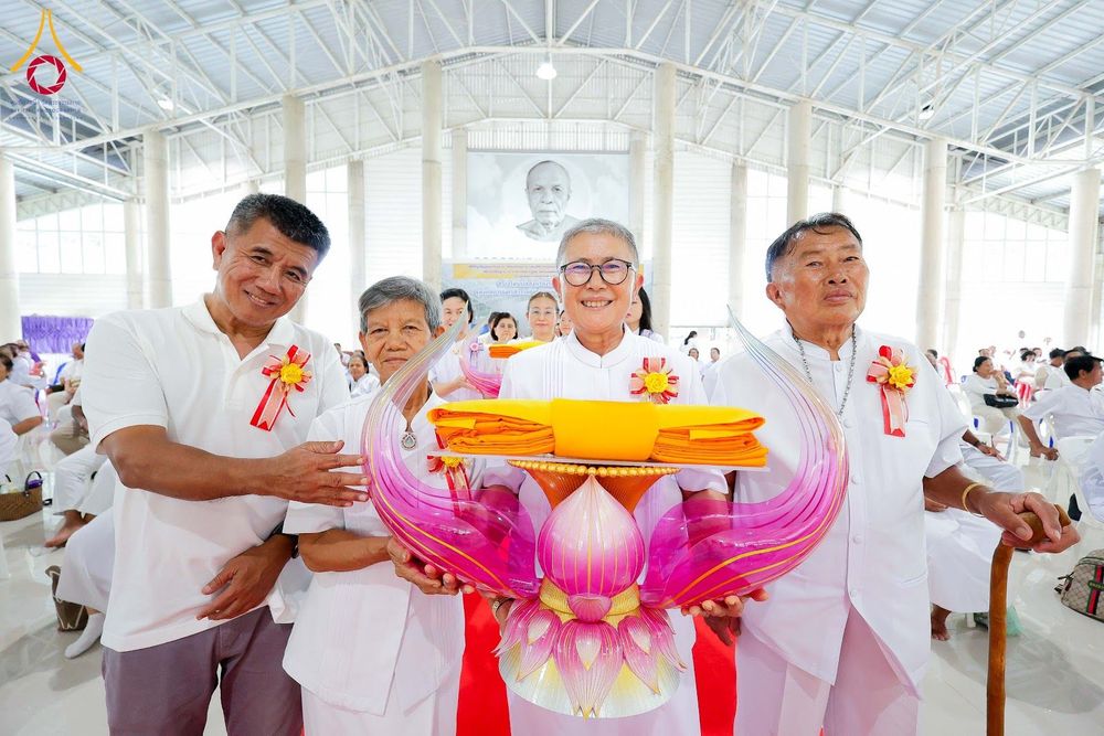 กลุ่มคนในชุดขาวถือพานพุ่มดอกบัวสีชมพูที่มีผ้าไตรจีวรวางอยู่ด้านบนเพื่อประกอบพิธีทางศาสนา