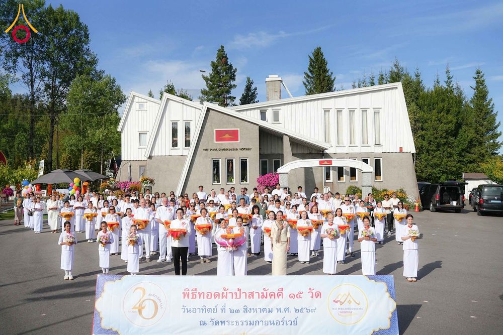 กลุ่มคนจำนวนมากสวมชุดสีขาวถ่ายภาพร่วมกันหน้าอาคารวัดพระธรรมกายนอร์เวย์ในวันจัดงานพิธีทอดผ้าป่าสามัคคี