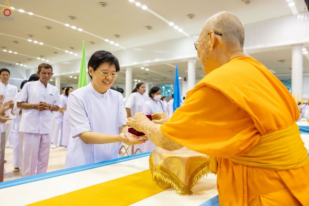 พระภิกษุสงฆ์มอบพระของขวัญให้แก่หญิงสาวในชุดสีขาวภายในห้องโถง