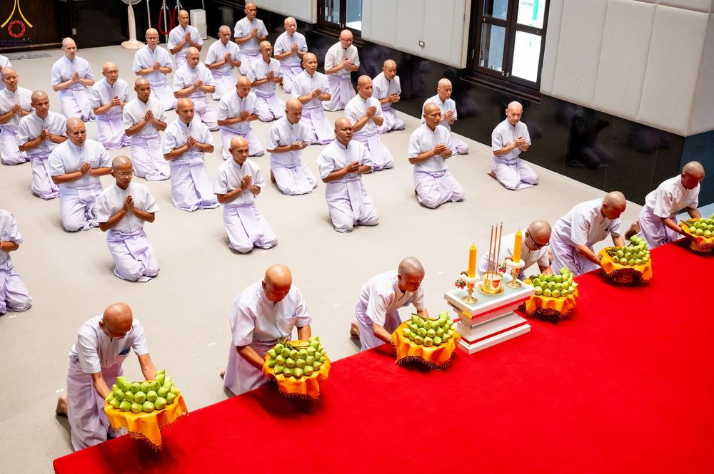กลุ่มผู้เข้าร่วมพิธีบรรพชาอุปสมบทในชุดสีขาวนั่งพนมมือและวางพานพุ่มดอกไม้ในพิธีทางศาสนา