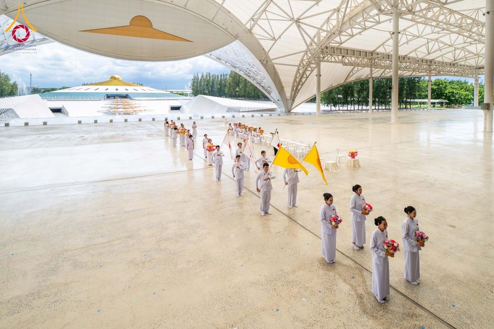 กลุ่มคนชุดขาวเดินถือธงและพานดอกไม้ในขบวนพิธีการภายในสภาธรรมกายสากล