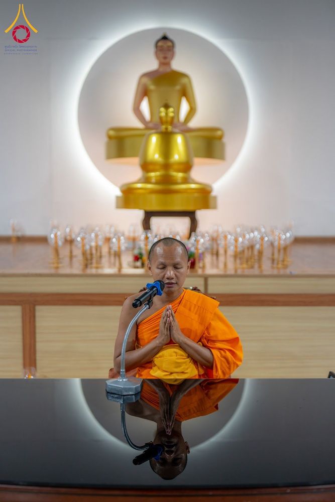 พระภิกษุประนมมือสวดมนต์หน้าไมโครโฟน โดยมีพระพุทธรูปเป็นฉากหลัง