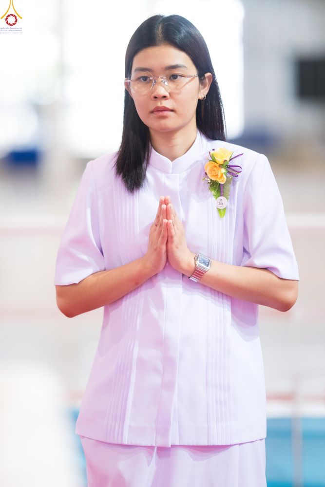 หญิงสาวสวมชุดสีขาวสวมแว่นตากำลังยืนพนมมืออย่างสำรวม