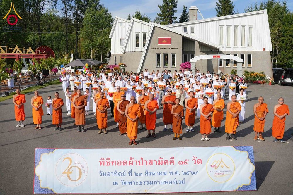 คณะสงฆ์ในจีวรสีส้มและสาธุชนในชุดขาวร่วมถ่ายภาพหมู่หน้าป้ายงานพิธีทอดผ้าป่าสามัคคี ณ วัดพระธรรมกายนอร์เวย์