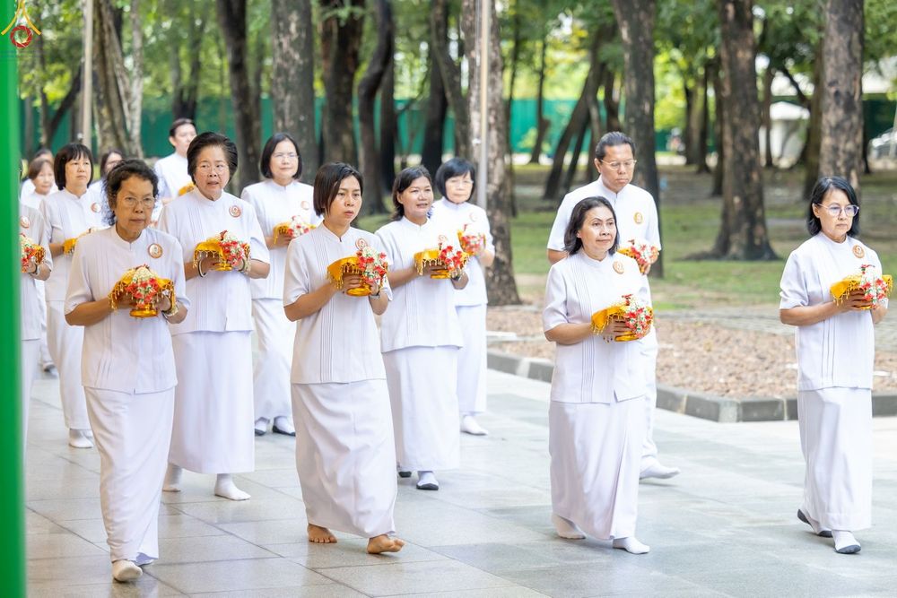 กลุ่มบุคคลสวมชุดขาวถือพานดอกไม้เดินเรียงแถวในพิธีกรรมทางศาสนา