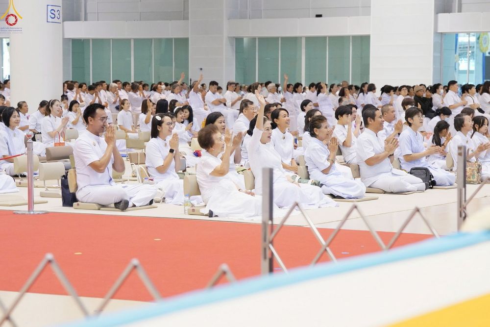 กลุ่มคนสวมชุดสีขาวนั่งพนมมือปฏิบัติธรรมภายในห้องโถงขนาดใหญ่