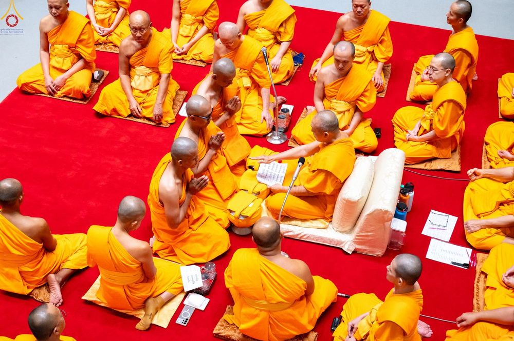 กลุ่มพระภิกษุและนาคในชุดจีวรสีเหลืองกำลังประกอบพิธีบรรพชาอุปสมบทภายในโบสถ์ที่มีพื้นปูด้วยพรมสีแดง