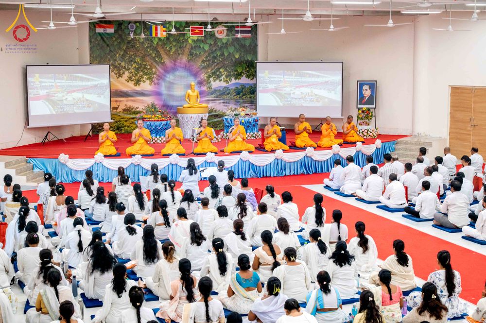 พระภิกษุสงฆ์และพุทธศาสนิกชนร่วมพิธีทางศาสนาภายในอาคารที่มีฉากหลังเป็นภาพต้นไม้และพระพุทธรูป