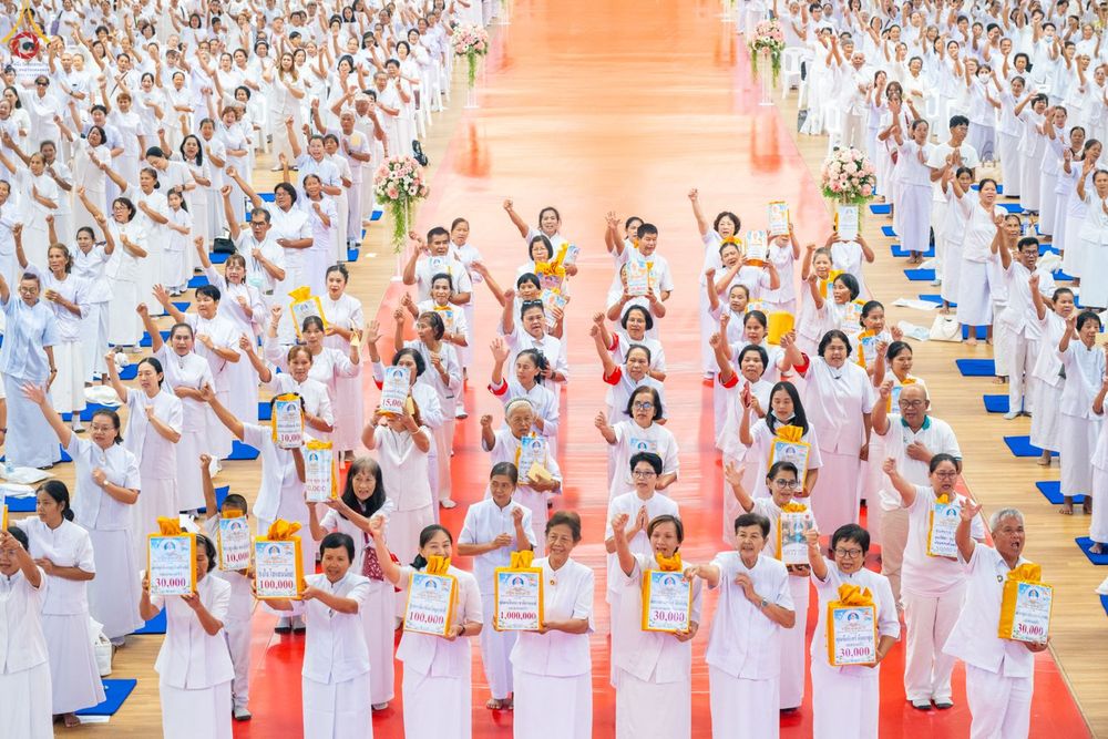 พุทธศาสนิกชนชุดขาวจำนวนมากถือป้ายทำบุญกฐินร่วมกิจกรรมสัมมนาภายในอาคาร