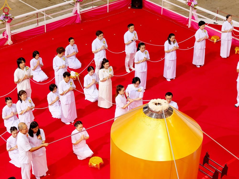 กลุ่มคนสวมชุดขาวประกอบพิธีทางศาสนาล้อมรอบประติมากรรมสีทองบนพื้นพรมสีแดง