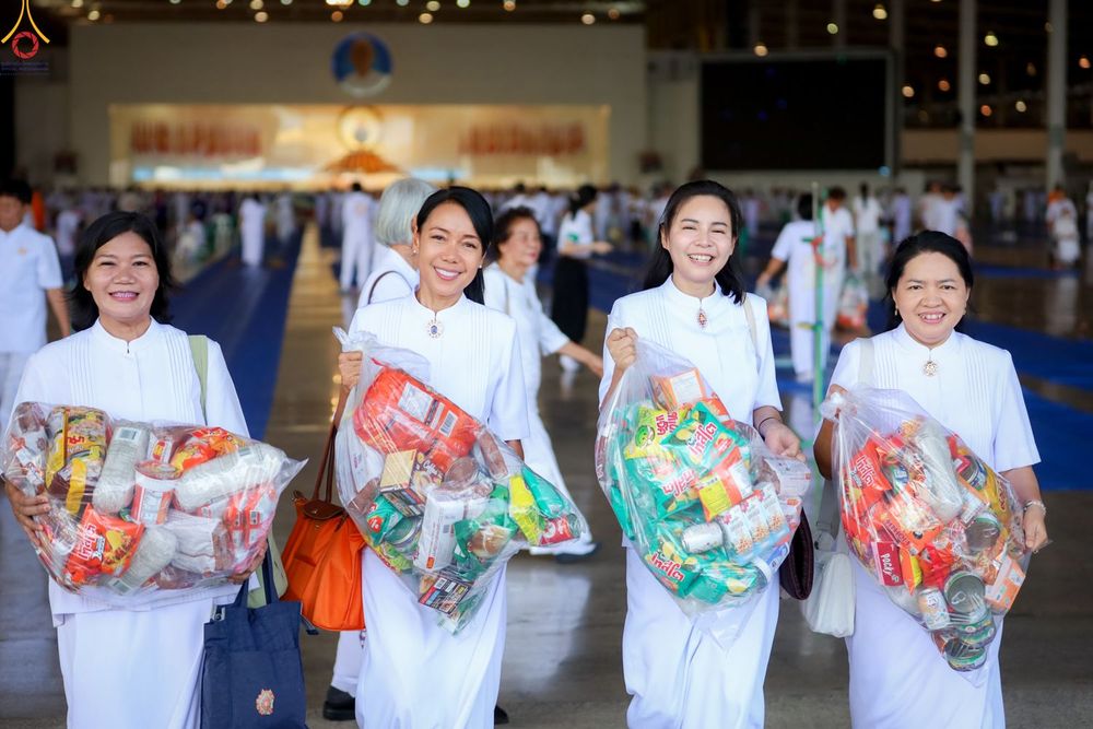 หญิงไทยสี่คนสวมชุดสีขาวถือถุงใส่ข้าวสารอาหารแห้งเพื่อเตรียมตักบาตรภายในอาคาร