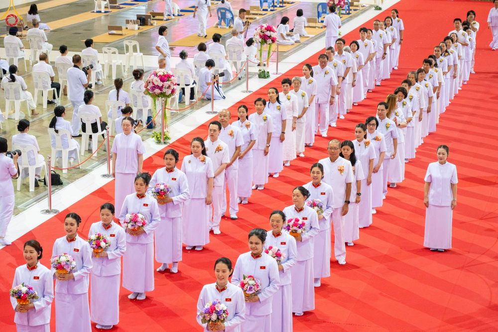 แถวผู้เข้าร่วมพิธีสวมชุดสีขาวเดินเรียงแถวบนพรมสีแดงภายในอาคาร