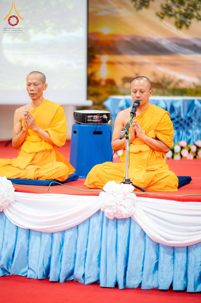 พระสงฆ์สองรูปนั่งพนมมือบนเวทีที่มีการตกแต่งด้วยผ้าสีฟ้าและสีขาว