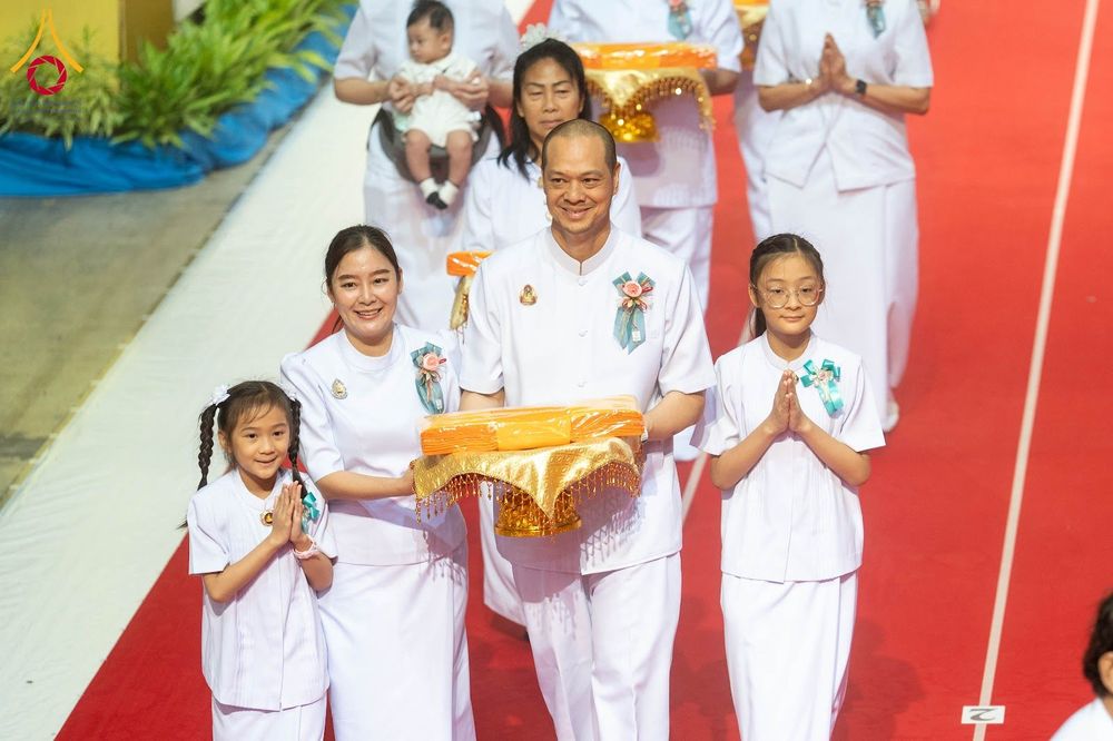 กลุ่มคนในชุดขาวเดินในขบวนอัญเชิญผ้าไตรสีเหลืองทองบนพรมแดง