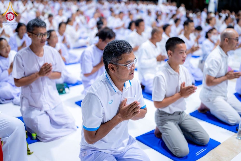 กลุ่มผู้เข้าร่วมโครงการอบรมสวมชุดสีขาวนั่งพนมมือปฏิบัติธรรมบนเบาะรองนั่งสีน้ำเงิน