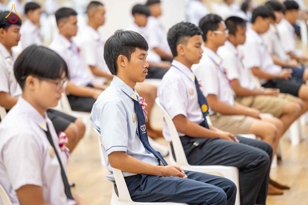 กลุ่มเยาวชนชายสวมชุดนักเรียนนั่งหลับตาทำสมาธิในห้องประชุม