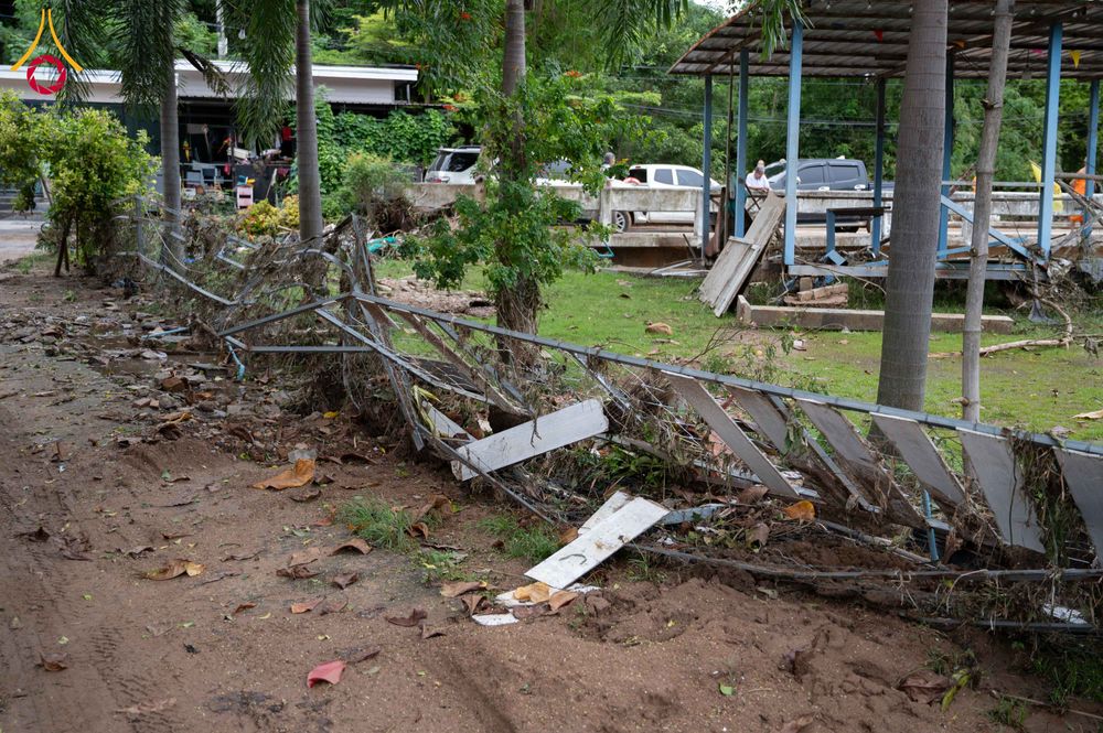 รั้วเหล็กที่พังเสียหายและเศษดินโคลนบนพื้นดินหลังเหตุการณ์น้ำท่วม