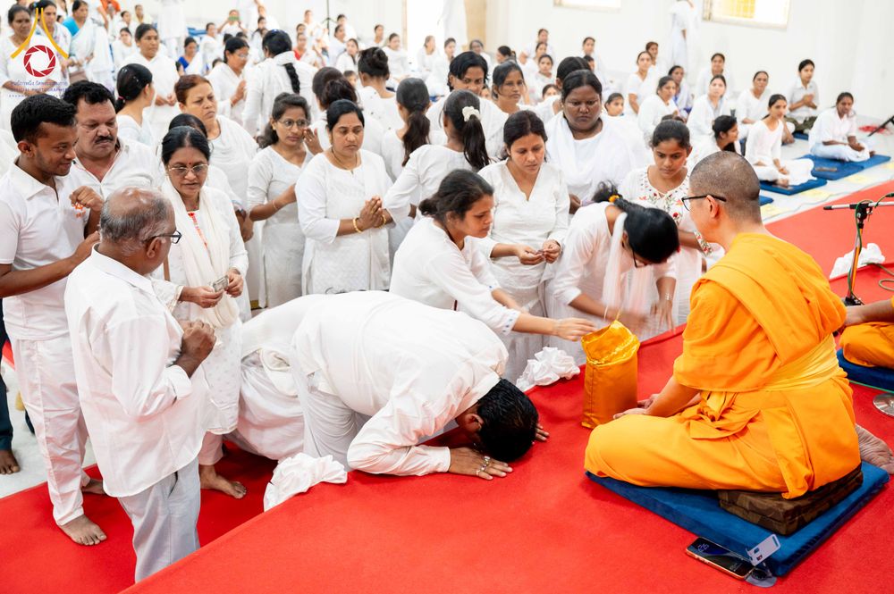 พุทธศาสนิกชนสวมชุดขาวกำลังถวายสังฆทานแด่พระสงฆ์บนเวทีปูพรมสีแดง