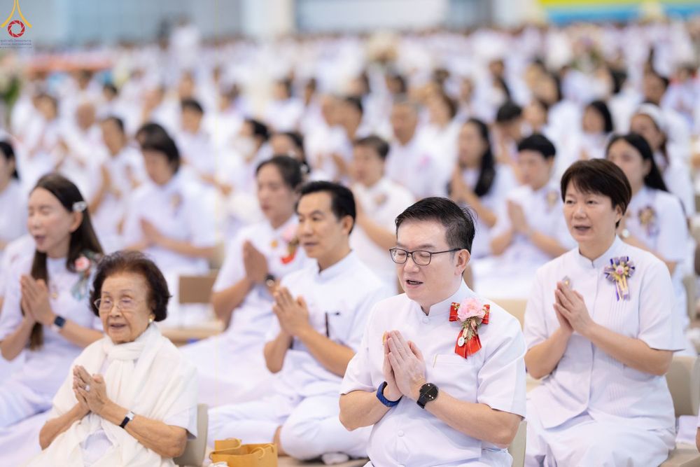 กลุ่มคนสวมชุดขาวนั่งพนมมือประกอบพิธีทางศาสนาภายในอาคาร