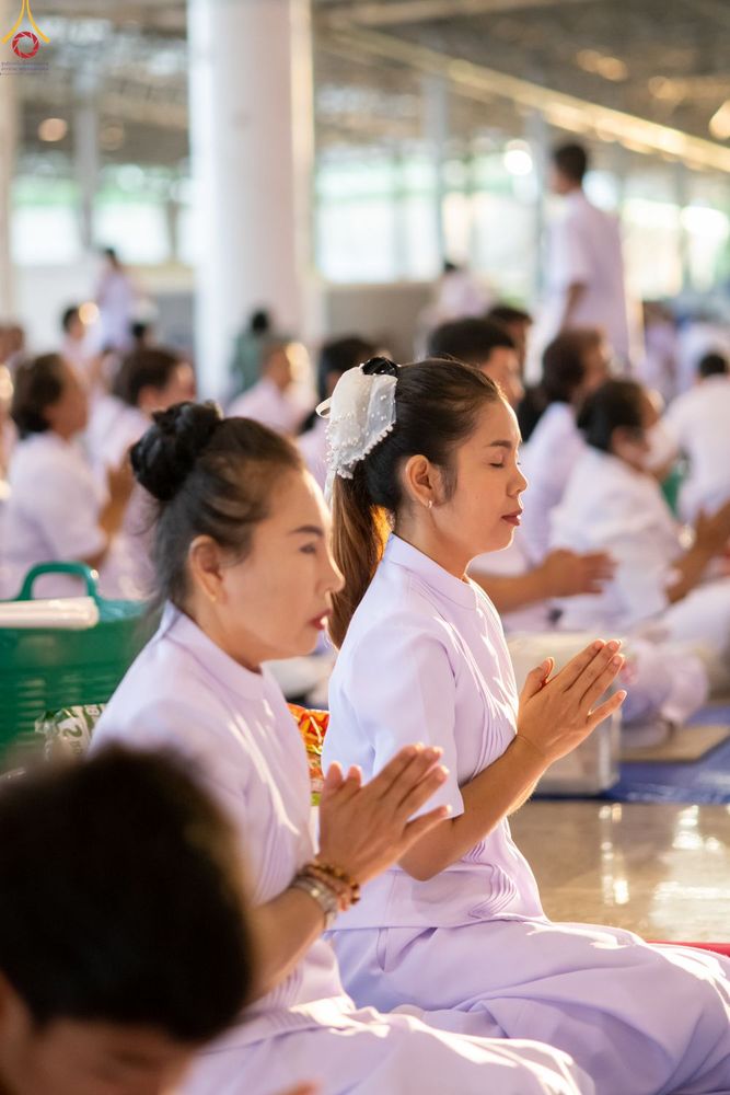 หญิงไทยแต่งกายชุดสีขาวนั่งพนมมือด้วยความสงบในพิธีตักบาตร ณ สภาธรรมกายสากล
