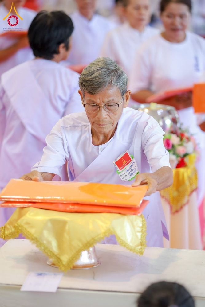 อุบาสิกาแก้วสวมชุดขาวกำลังวางผ้าไตรจีวรสีส้มบนพานพุ่มสีทอง
