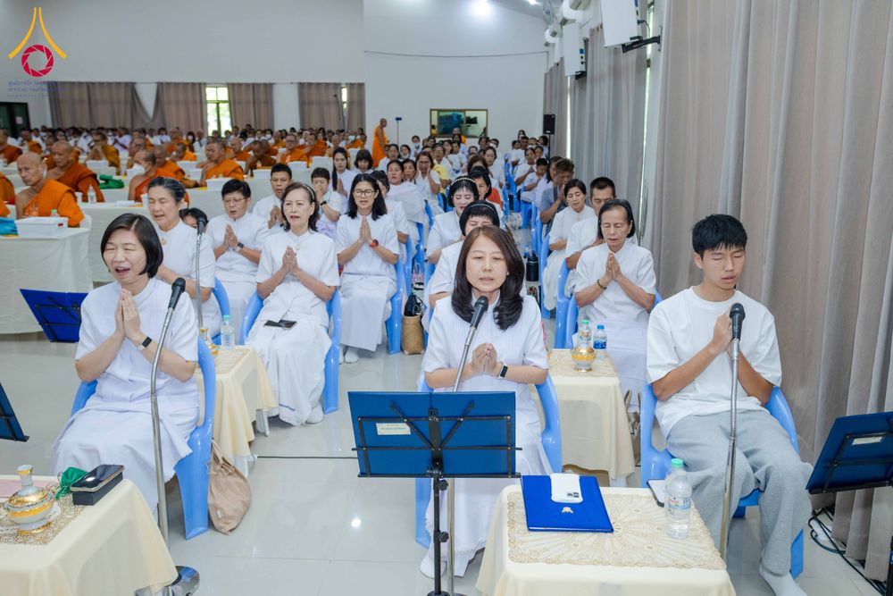 กลุ่มคนสวมชุดขาวนั่งพนมมือฟังการบรรยายในห้องสัมมนาที่มีพระภิกษุสงฆ์ร่วมงาน