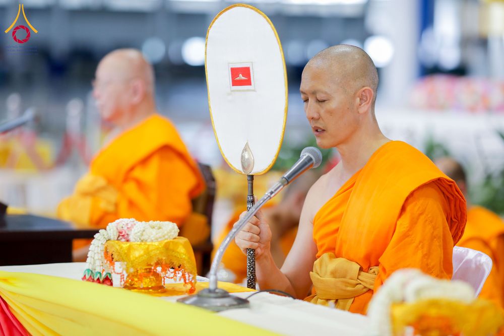พระภิกษุถือพัดยศและพูดผ่านไมโครโฟนในงานพิธีทางศาสนา