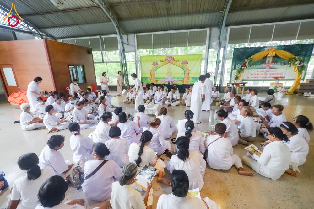 กลุ่มคนสวมชุดขาวนั่งล้อมวงทำกิจกรรมภายในอาคาร