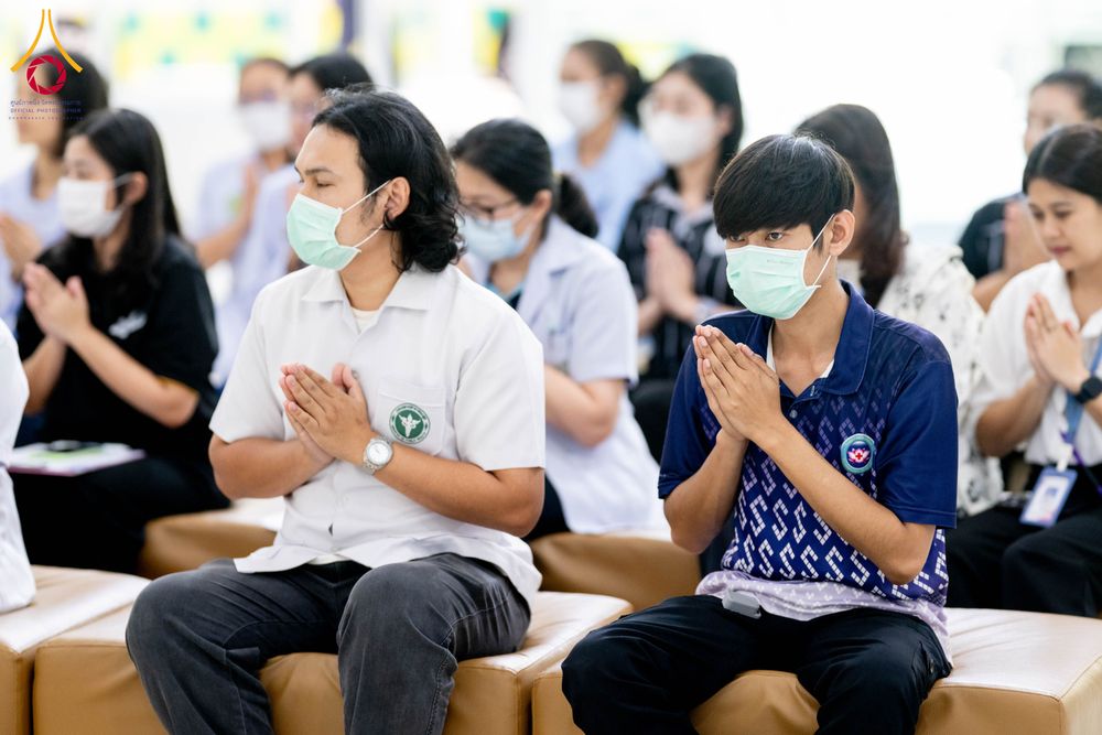 กลุ่มบุคคลสวมหน้ากากอนามัยนั่งพนมมือในลักษณะสำรวมภายในอาคาร
