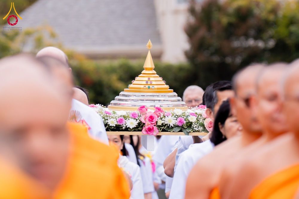 กลุ่มคนและพระภิกษุสงฆ์กำลังอัญเชิญพานพุ่มประดิษฐานพระบรมสารีริกธาตุจำลองสีทองประดับดอกไม้ในพิธีกรรมทางศาสนา
