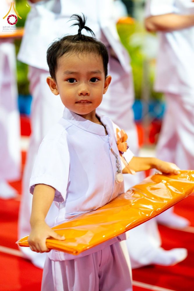 เด็กชายสวมชุดขาวถือผ้าไตรสีเหลืองทองในงานพิธีทางศาสนา