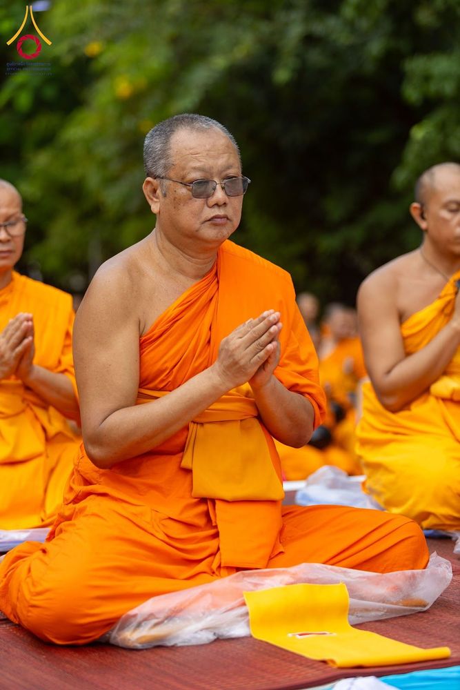 พระสงฆ์สวมจีวรสีส้มสวมแว่นตานั่งพนมมือประกอบพิธีกรรมทางศาสนา