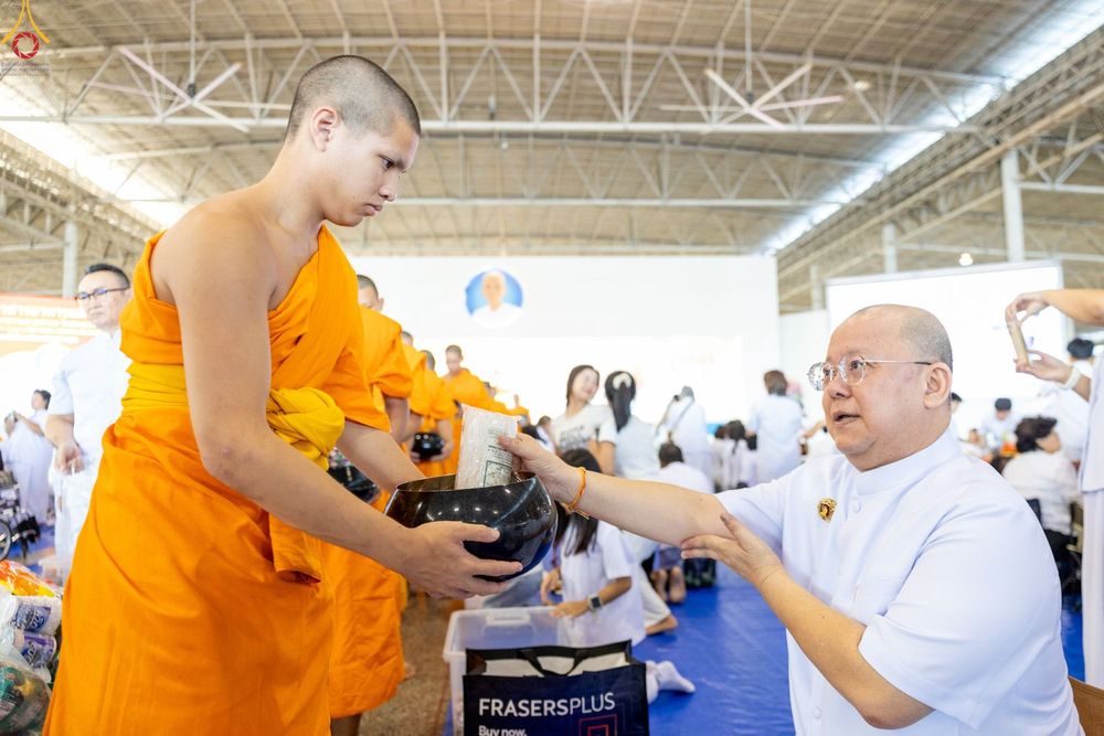 ชายสวมชุดขาวกำลังใส่ข้าวสารลงในบาตรของพระภิกษุสงฆ์ในพิธีตักบาตร