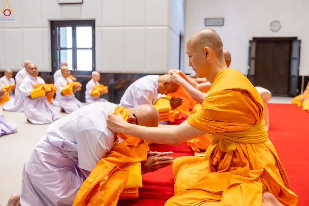 พระภิกษุสงฆ์กำลังมอบผ้าไตรจีวรให้แก่นาคในพิธีบรรพชาอุปสมบทภายในโบสถ์