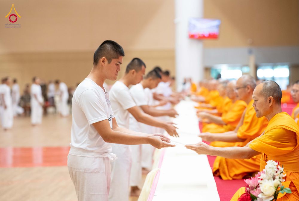 นักเรียนนายสิบตำรวจสวมชุดขาวกำลังรับมอบสิ่งของจากพระสงฆ์ในพิธีทางศาสนา