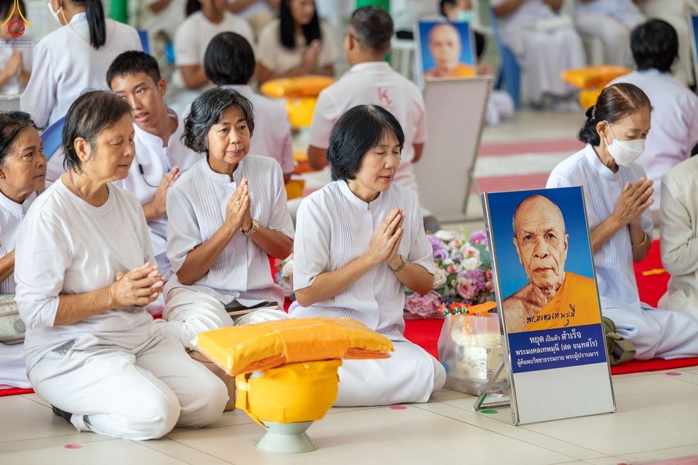 กลุ่มคนสวมชุดขาวนั่งพนมมือในพิธีทางศาสนา โดยมีภาพถ่ายพระมงคลเทพมุนีตั้งอยู่ด้านหน้า