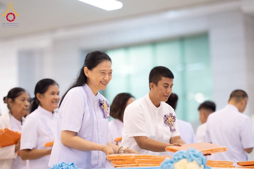 กลุ่มคนสวมชุดสีขาวกำลังจัดเตรียมผ้าไตรในพิธีทอดผ้าป่าด้วยความตั้งใจและมีรอยยิ้ม