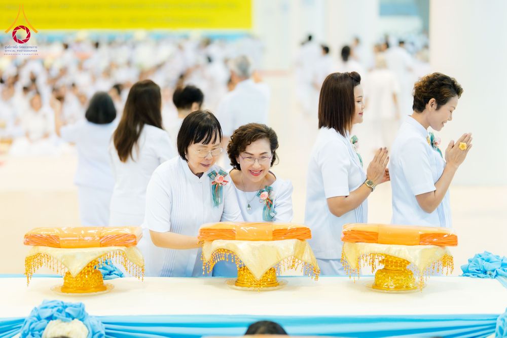 กลุ่มผู้หญิงในชุดสีขาวกำลังประกอบพิธีทอดผ้าป่าโดยมีพานวางผ้าไตรสีเหลืองทองวางอยู่บนโต๊ะ