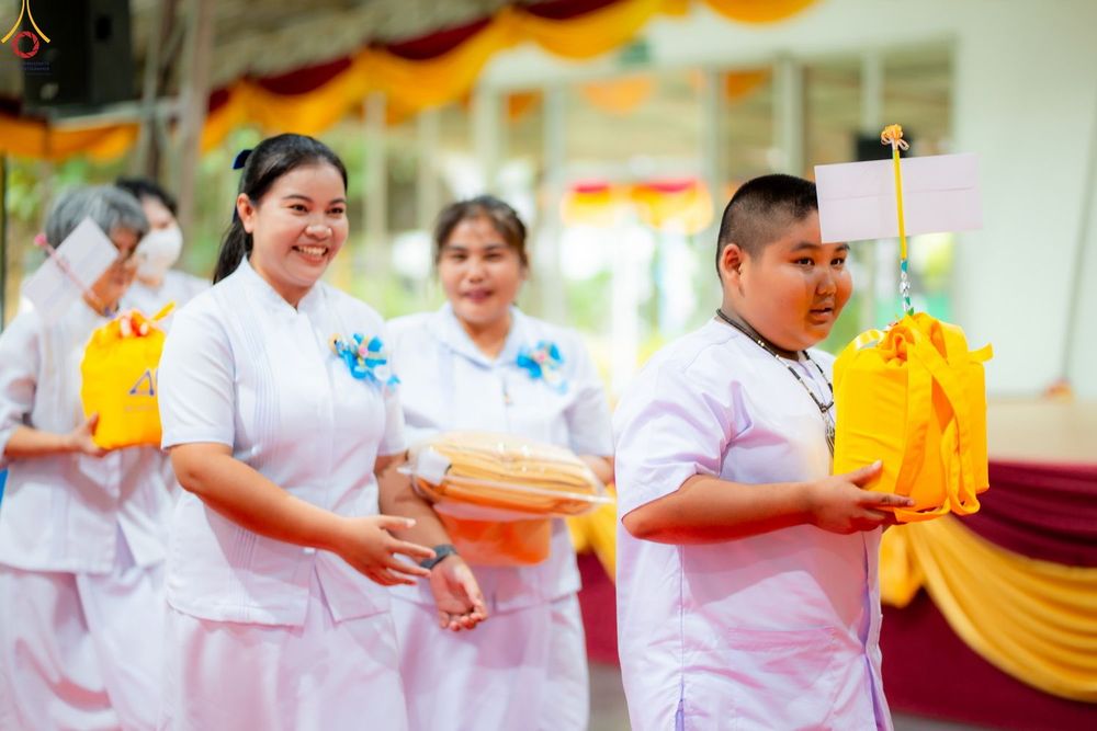 กลุ่มคนสวมชุดสีขาวถือถุงสังฆทานสีเหลืองเดินในงานพิธี