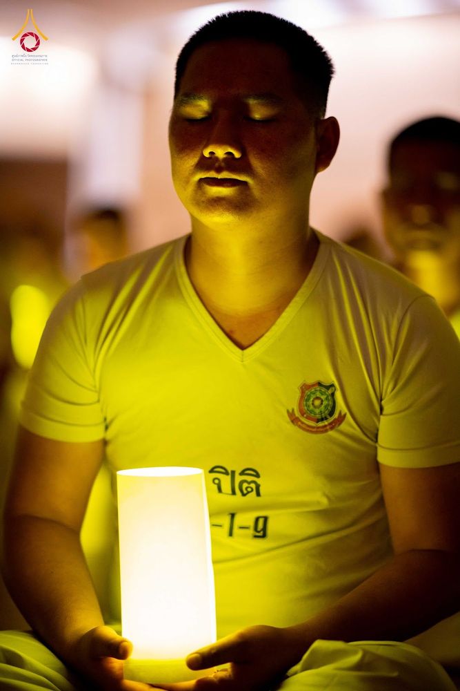 ชายสวมเสื้อยืดสีขาวนั่งหลับตาทำสมาธิและถือเทียนส่องสว่างในมือ