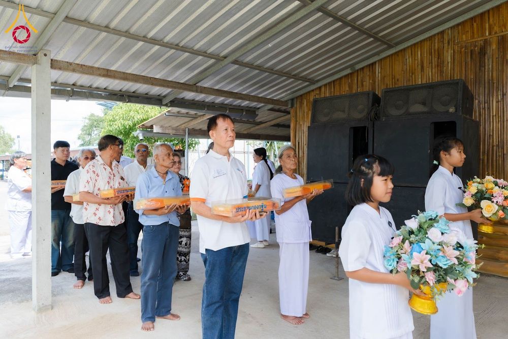 กลุ่มคนยืนเรียงแถวถือกล่องผ้าไตรและพานดอกไม้เพื่อเข้าร่วมพิธีทางศาสนา