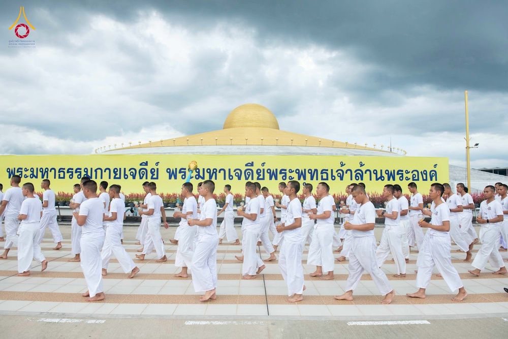 กลุ่มชายสวมชุดขาวเดินแถวเรียงหน้ากระดานหน้าพระมหาธรรมกายเจดีย์