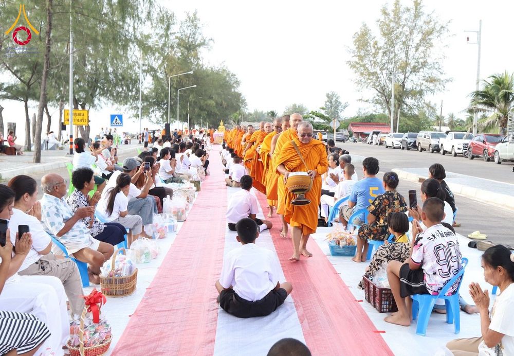 พระสงฆ์ในจีวรสีส้มกำลังเดินรับบิณฑบาตจากประชาชนที่นั่งรอใส่บาตรอยู่ริมถนนใกล้ชายหาด