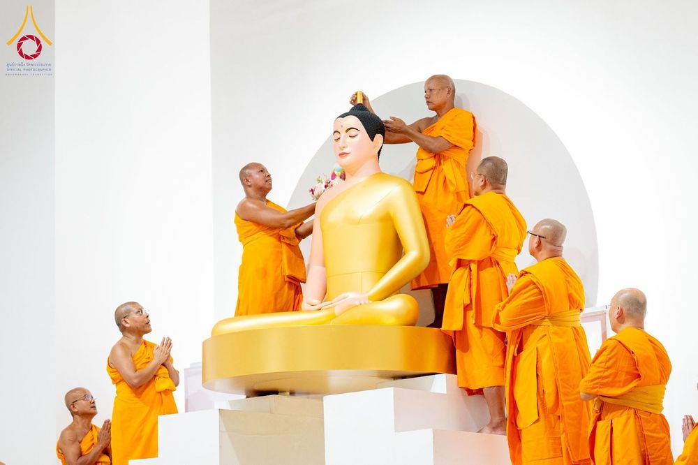 พระภิกษุสงฆ์ในจีวรสีส้มกำลังประกอบพิธีบรรจุพระบรมสารีริกธาตุบนส่วนเกศของพระพุทธรูปองค์ใหญ่สีทอง