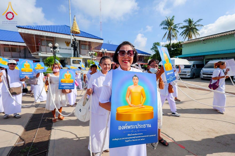 กลุ่มคนสวมชุดขาวถือป้ายภาพพระพุทธรูปสีทองเดินขบวนกลางแจ้ง