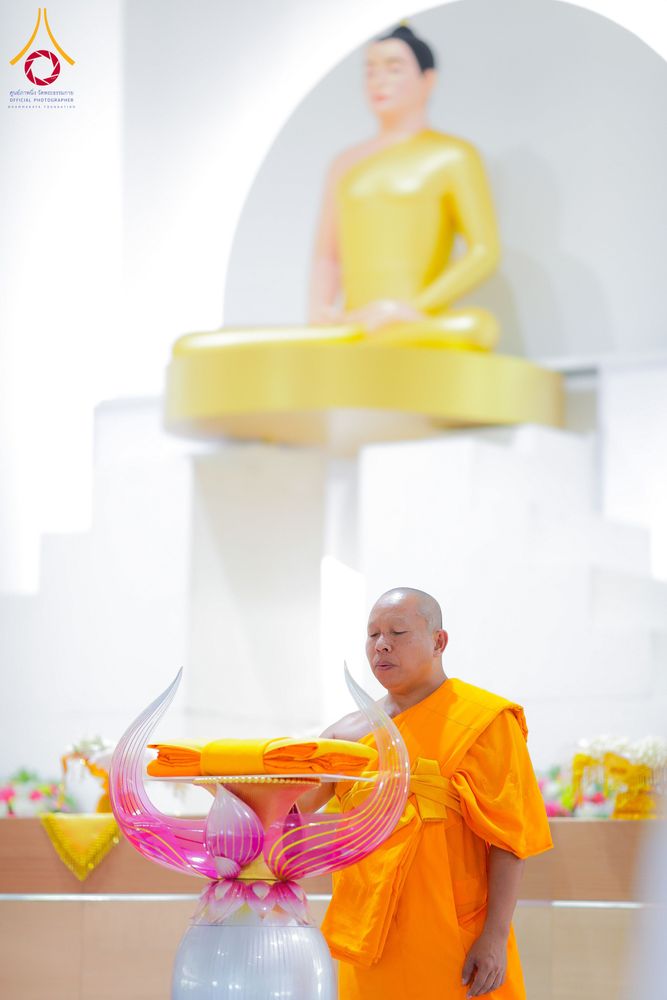พระสงฆ์กำลังประกอบพิธีหน้าพานผ้าไตร โดยมีพระพุทธรูปสีทองเป็นฉากหลัง
