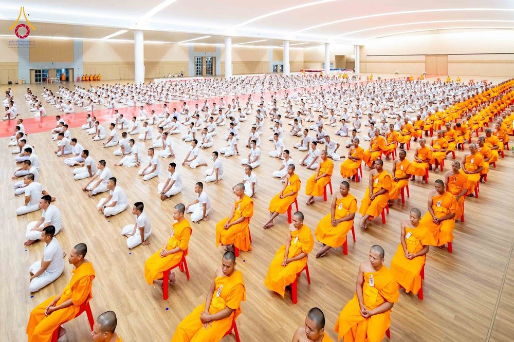 กลุ่มผู้เข้าร่วมโครงการบรรพชาในชุดจีวรสีส้มและชุดขาวนั่งเรียงแถวในหอประชุม