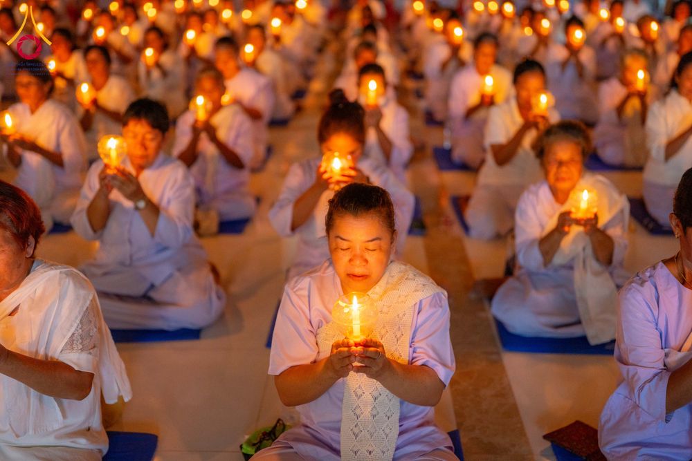 กลุ่มผู้เข้าร่วมโครงการอบรมอุบาสิกาแก้วสวมชุดสีขาวนั่งสมาธิถือเทียนสว่างไสวในพิธีกรรมทางศาสนา