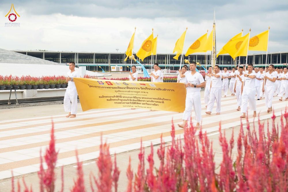 กลุ่มนักเรียนนายสิบตำรวจสวมชุดขาวเดินถือป้ายโครงการและธงสีเหลืองในขบวนแถว